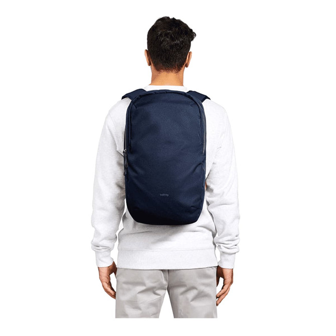 A person wearing a navy blue backpack, featuring padded shoulder straps and a simple design. The backpack has a logo.