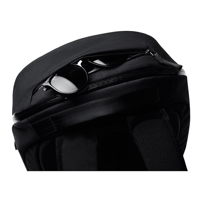 A black backpack with a zippered compartment, containing a pair of sunglasses. It features a logo on the exterior.