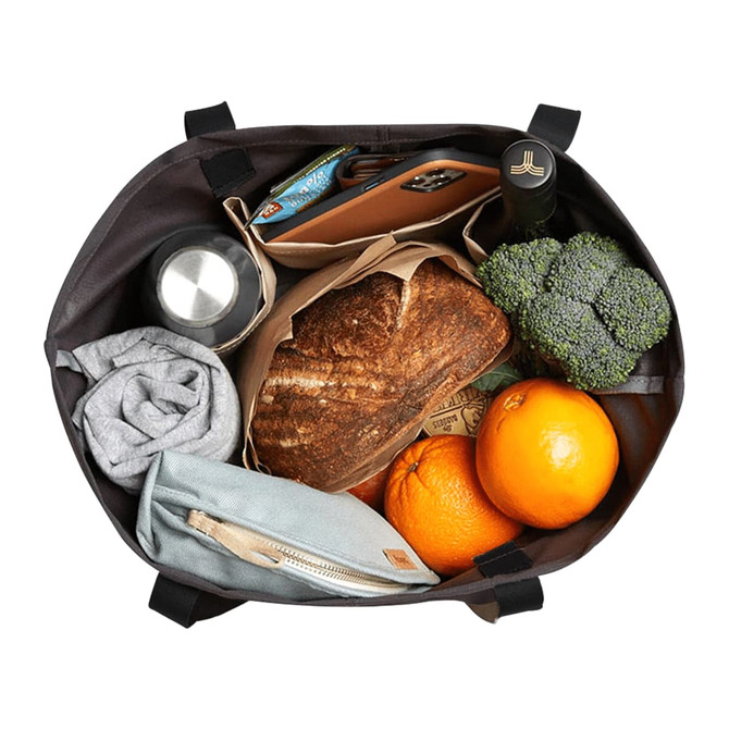 A Bellroy Market Tote in dark colour, filled with groceries including broccoli, oranges, a drink bottle, and a loaf of bread.