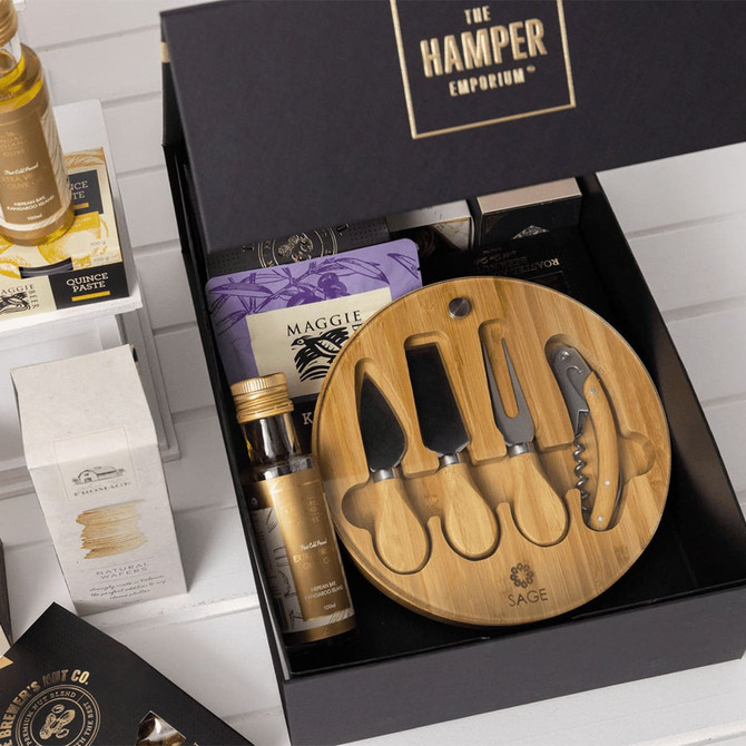 A gourmet gift pack featuring a bamboo cheese board set, assorted snacks, and a selection of condiments in a black box.