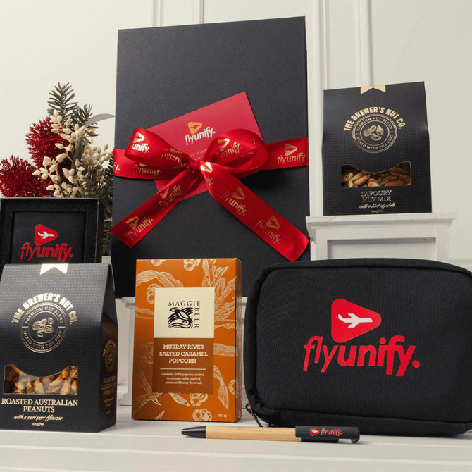 A gift box with a red ribbon, containing snacks, a black pouch, and a pen, all featuring a logo.