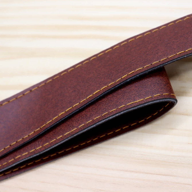 A brown leather strap with yellow stitching, laid on a wooden surface. The strap has a smooth finish and a sturdy appearance.