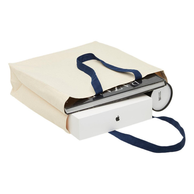 A cream heavy-duty canvas tote with navy handles, filled with various items including books and a box.