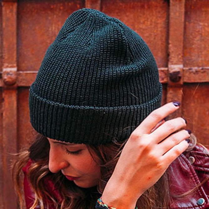 A dark green Woolly Beanie being worn by a person, featuring a ribbed texture and a snug fit.