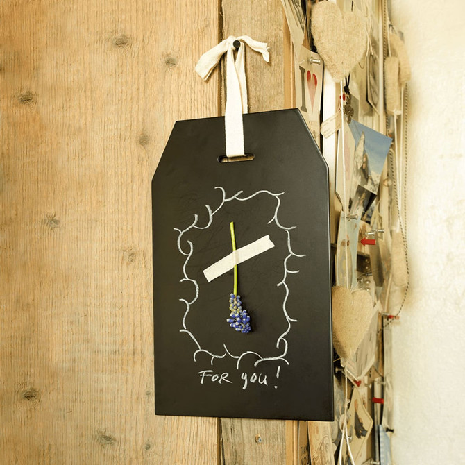 A blackboard tag with a decorative border, featuring a white ribbon and a simple flower arrangement.