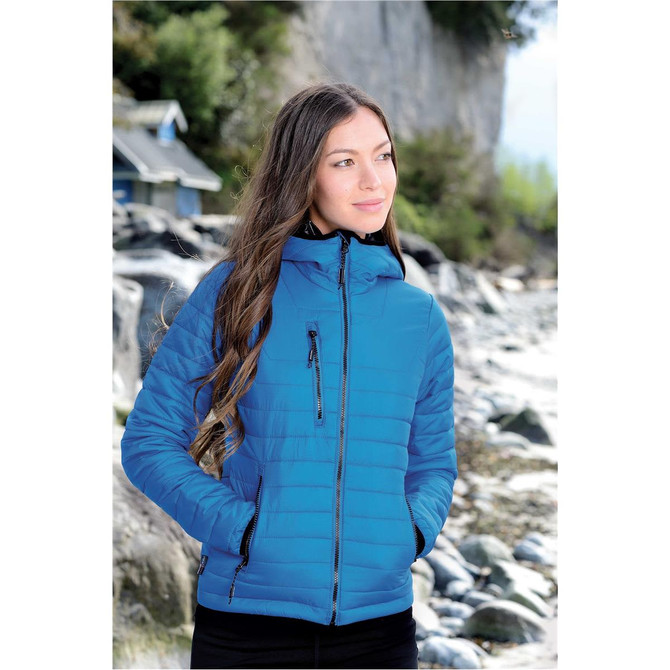 A women's puffer jacket in blue with a fitted hood and zippered pockets, featuring a branded logo.
