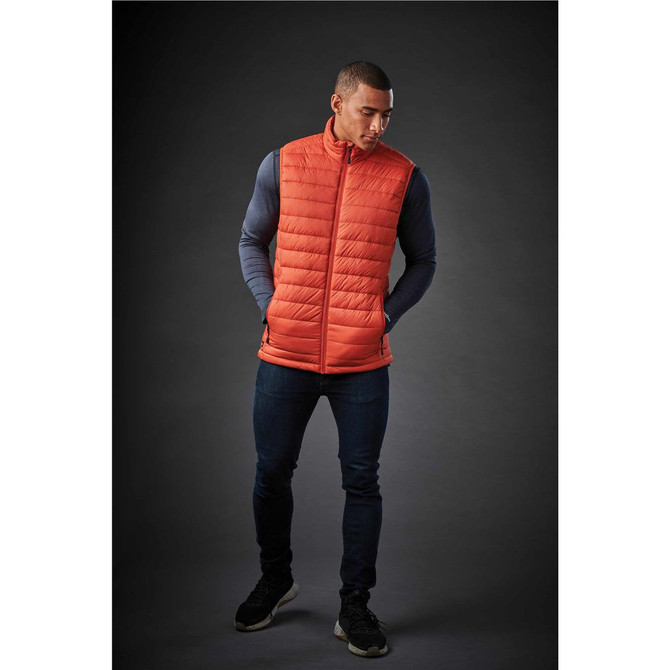 An orange thermal vest worn by a man, featuring a quilted design and a branding logo.
