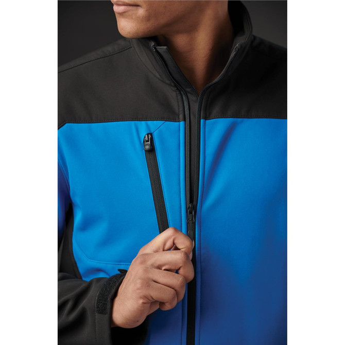 A blue and black softshell jacket with zippered pockets, featuring a person adjusting the zipper.