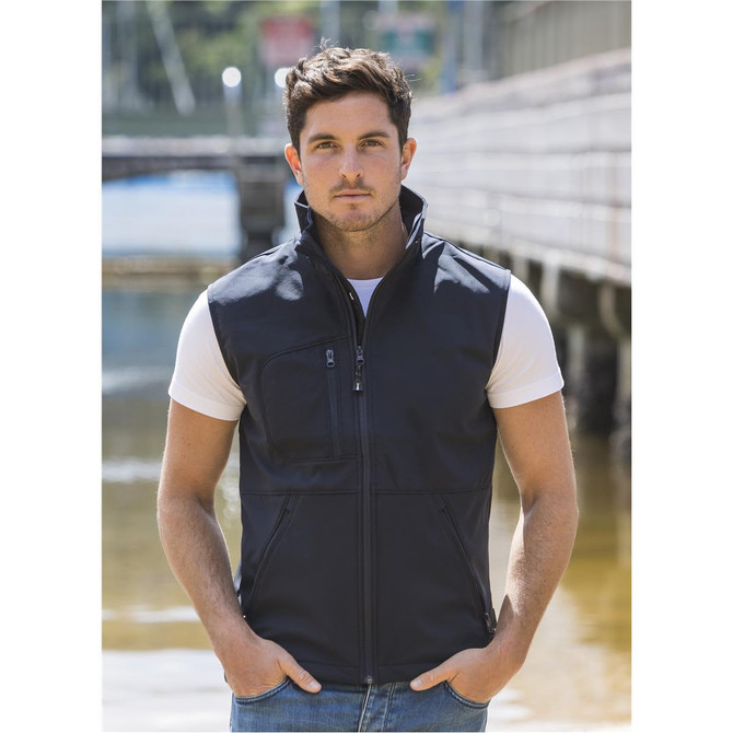 A black softshell vest with a zip front, featuring pockets and a high collar, worn by a man by the water.