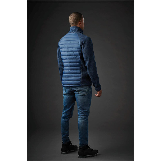 A man wearing a blue hybrid jacket, featuring a quilted front and textured back, paired with jeans and boots.