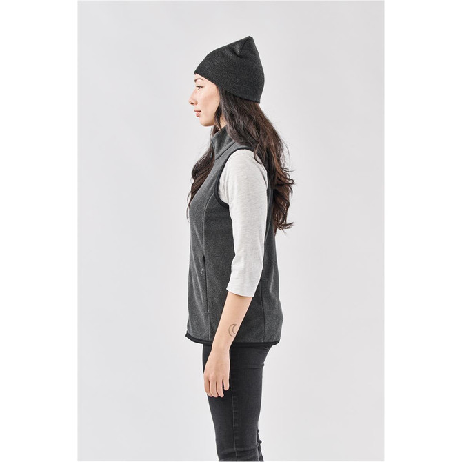 A woman in profile wearing a dark grey beanie and a light grey long-sleeve top, paired with a grey vest.