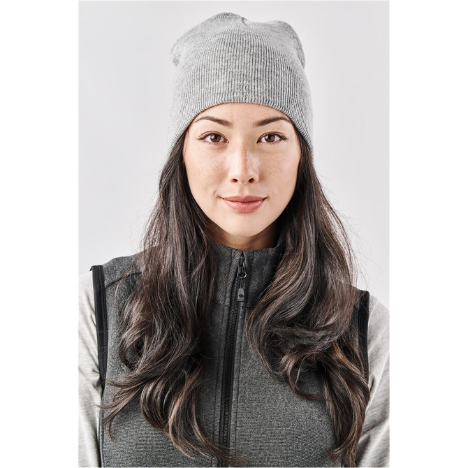 A grey knit beanie displayed on a model with long hair, featuring a simple design and a logo.