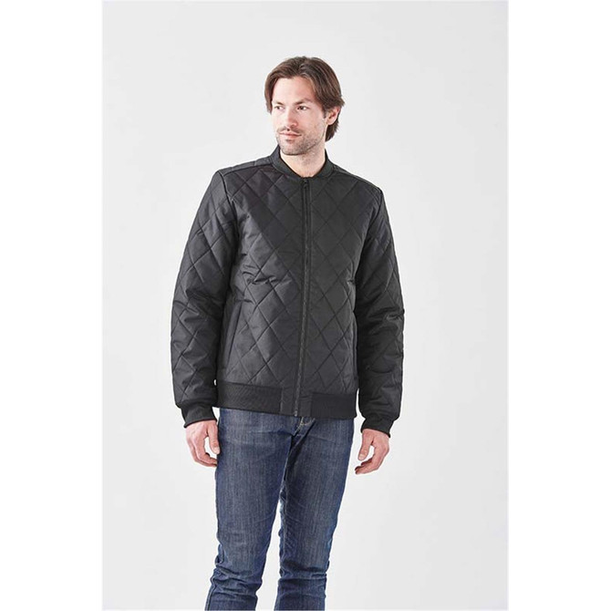 A man wearing a black quilted thermal jacket with a zip front and ribbed cuffs, standing against a plain background.