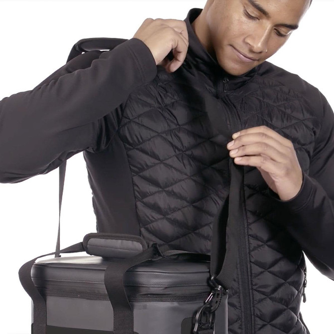 A person wearing a black padded jacket adjusts the strap of a black cooler bag that has a logo.