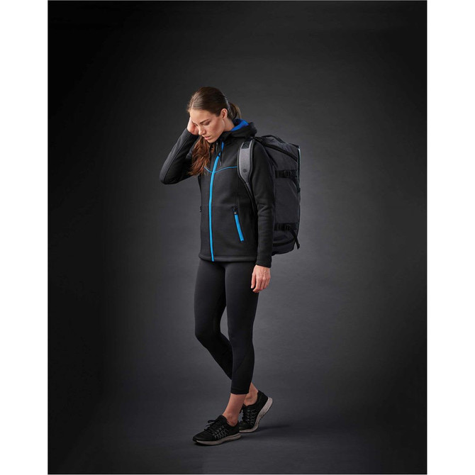 A woman in a black jacket with blue accents and leggings, carrying a duffel bag on her back.