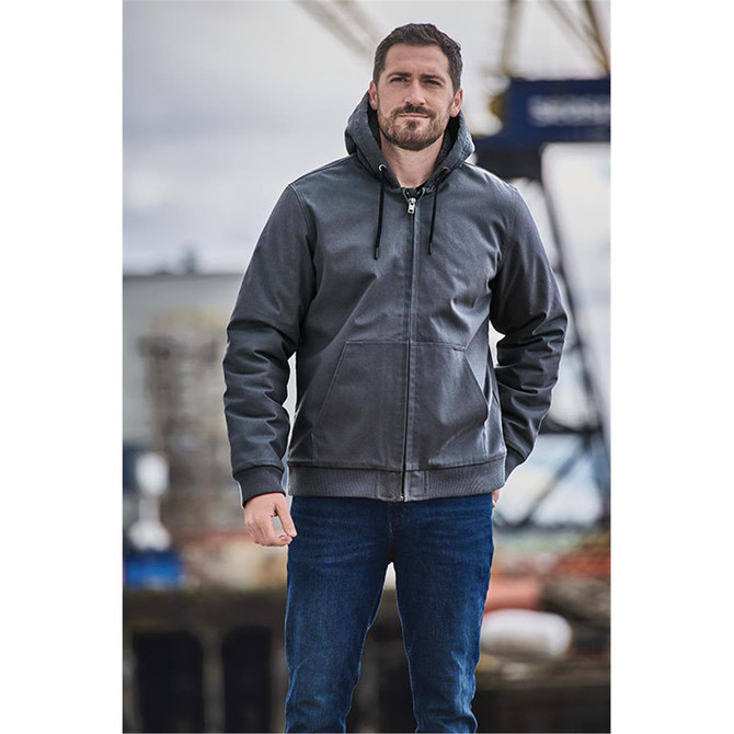 A man stands wearing a grey hooded jumper. The hoodie features a logo and has a zipper and drawstring.