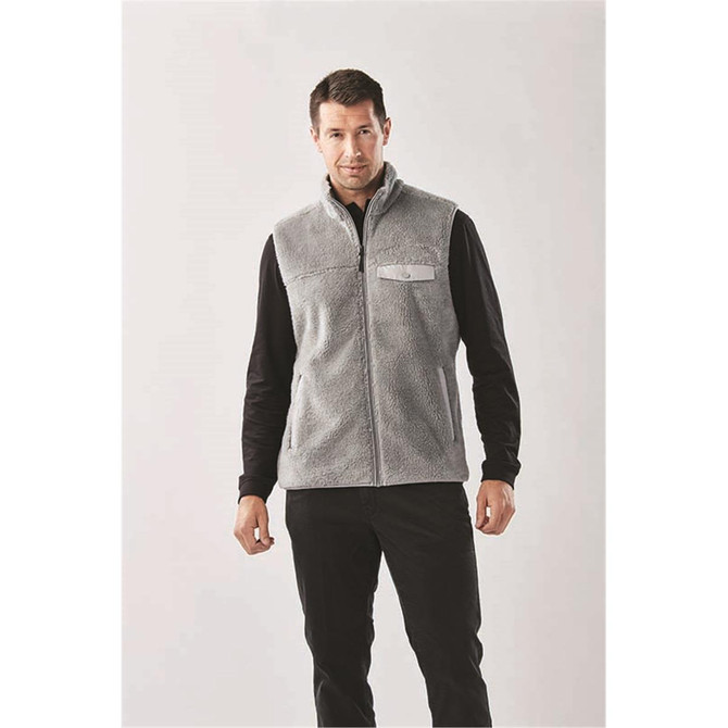 A grey men's fleece vest with a zip front and a logo on the chest, styled with a black long sleeve shirt.