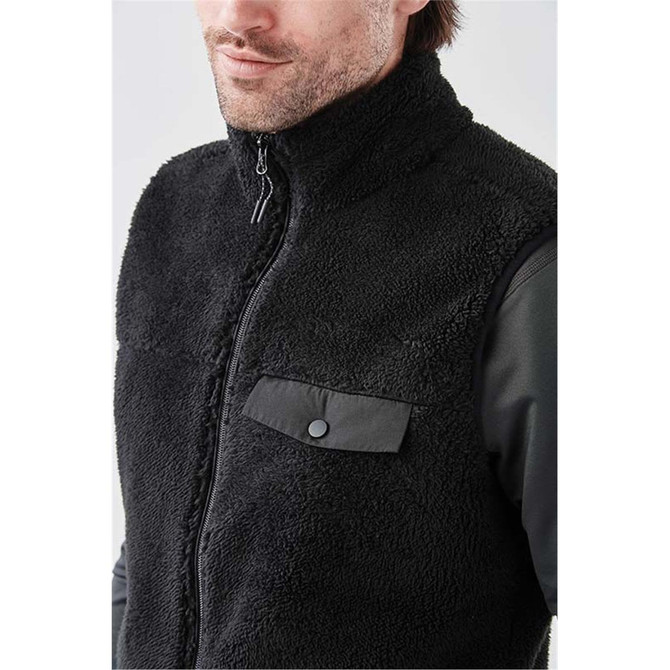 A men's black Sherpa fleece vest featuring a zip-up front and a snap-button pocket. The vest has a logo.