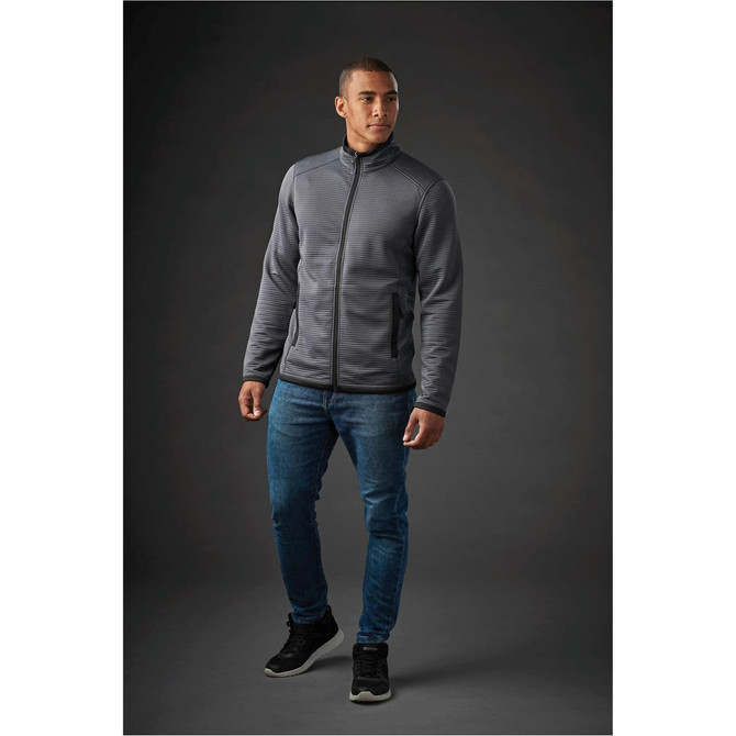 A man wearing a grey Men's Andorra Jacket, paired with blue jeans and black shoes, standing against a dark background.