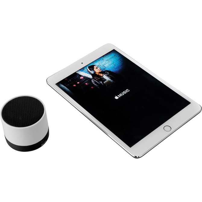 A cylindrical Bluetooth speaker in black and white, alongside a tablet displaying music content.