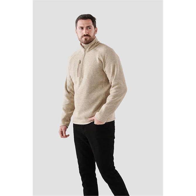 A men's beige pullover with a quarter zip, featuring a logo, styled with black pants.