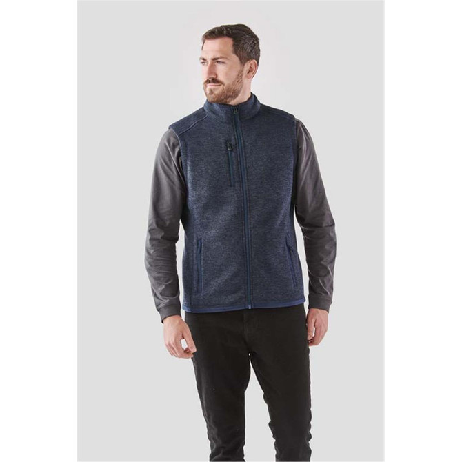 A man models a navy blue fleece vest with a full zip, featuring a logo and side pockets.