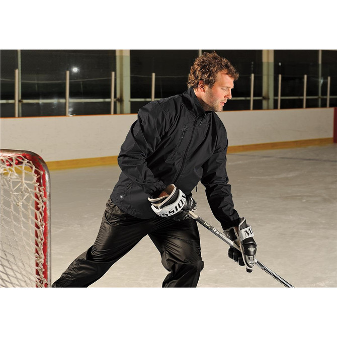 A man wearing a black Men's Axis Thermal Jacket on an ice rink, holding a hockey stick. The jacket has a logo.