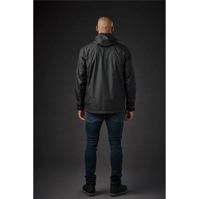 A man wearing a black rain jacket, viewed from the back, paired with dark jeans and shoes. The jacket has a hood and logo.