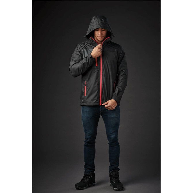 A man wearing a black rain jacket with red accents and a hood, standing against a dark background. The jacket features a logo.