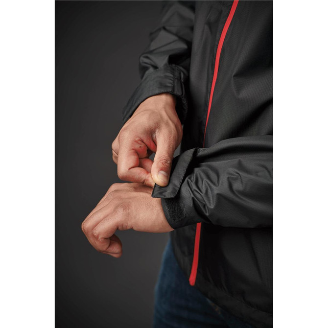 A close-up of a person adjusting the cuff of a black rain jacket with red accents. The jacket features a logo.