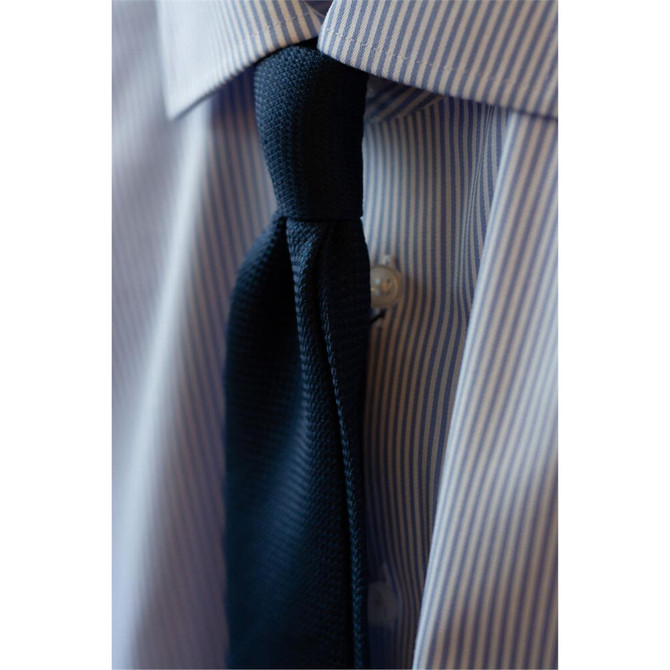 A close-up of a button-up shirt featuring blue and white stripes, paired with a dark tie.