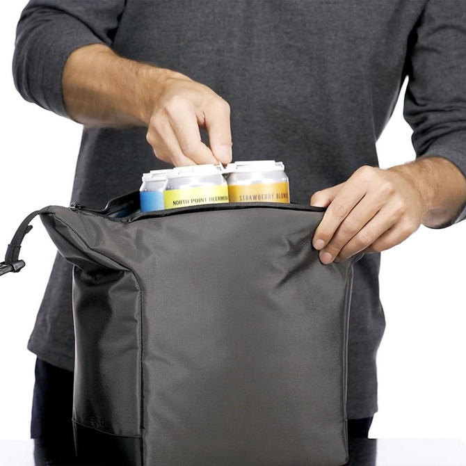 A grey cooler bag with cans being placed inside, featuring a zippered opening and a hand reaching in.