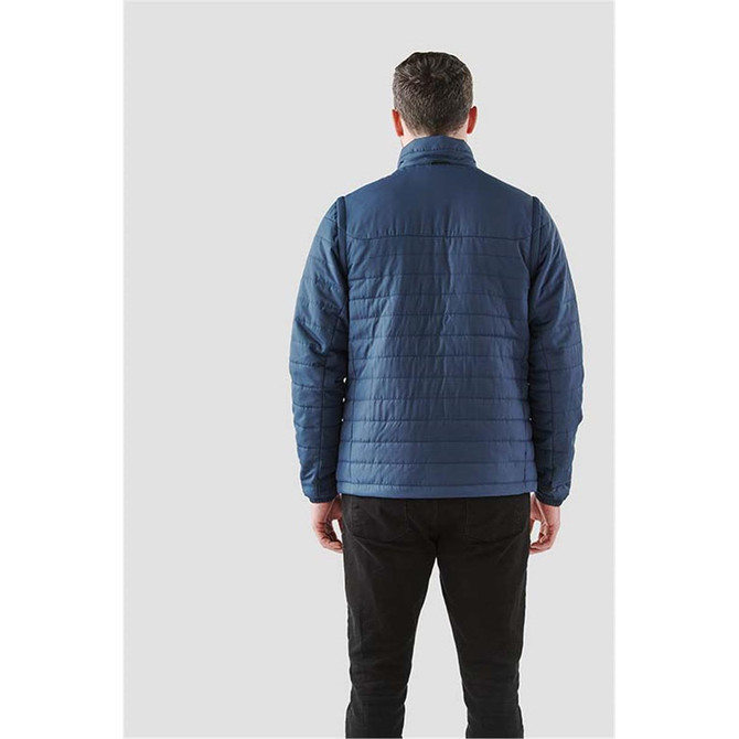 A man wearing a navy blue, quilted 5-in-1 system jacket, viewed from the back. The jacket features a high collar.