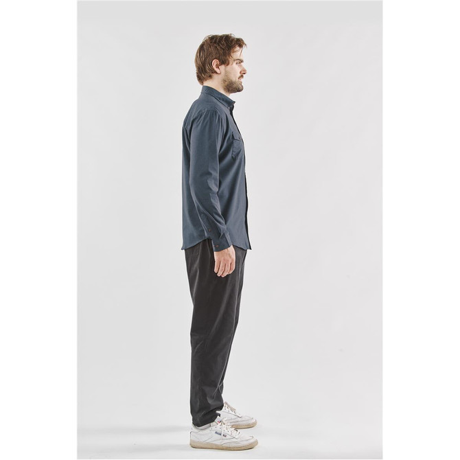A man in a navy blue quick dry shirt stands sideways, paired with black trousers and white sneakers.