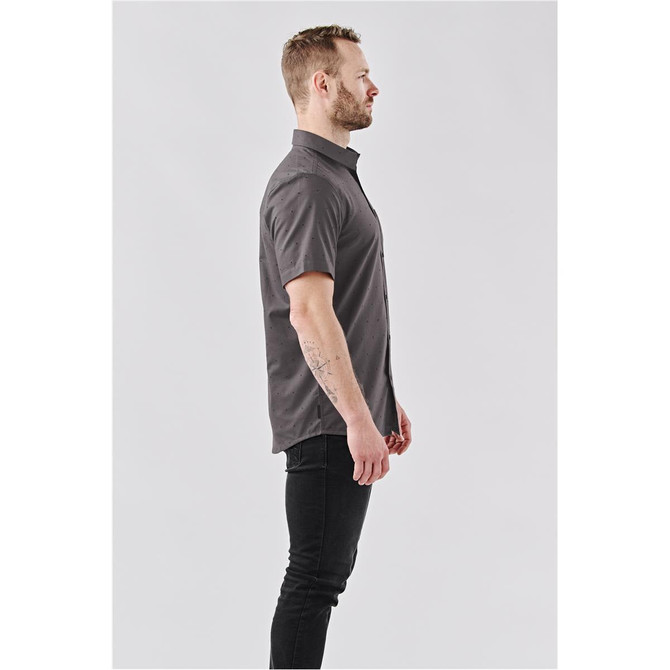 A man models a short-sleeved, charcoal grey button-up shirt with a logo on the chest.