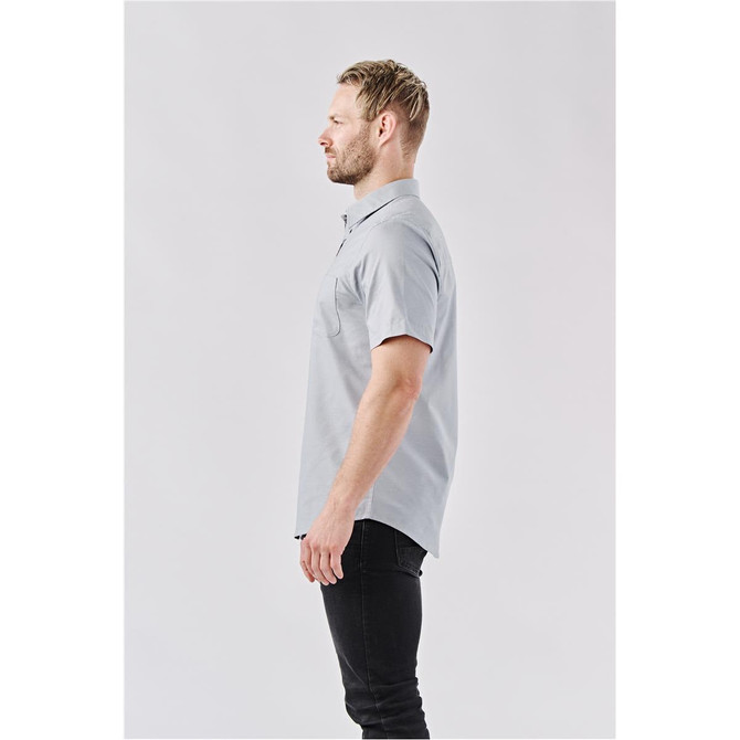 A grey men's short-sleeve button-up shirt displayed on a model from the side. The shirt features a pocket and has a branding logo.