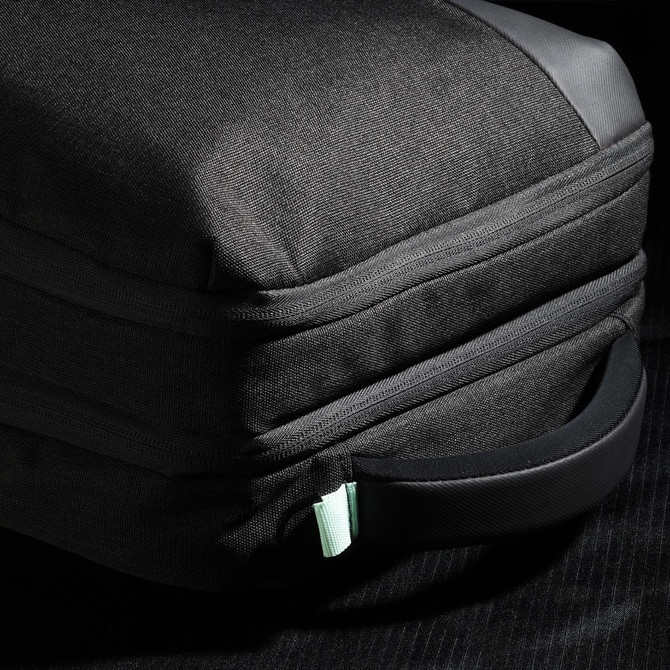 A black backpack with a textured exterior and a mint green zipper pull, featuring a side handle.