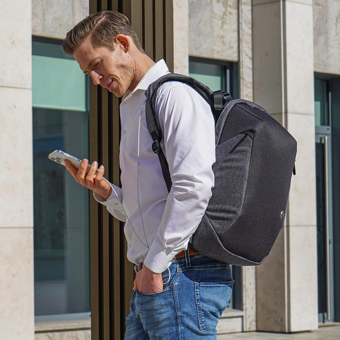 A man wearing a grey Swissdigital Cosmo 3.0 backpack checks his phone outdoors. The backpack features a logo.