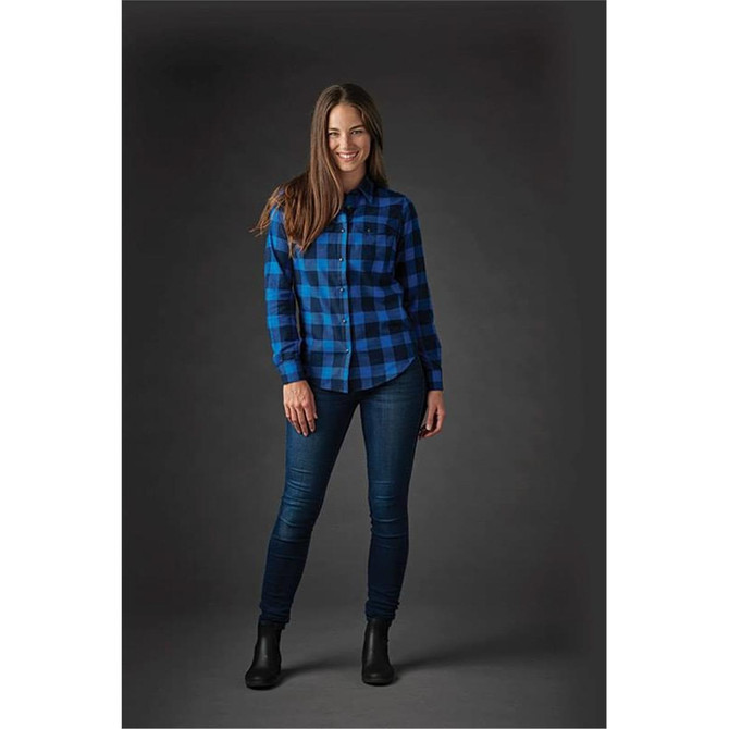 A woman wearing a blue and black checked button-up shirt and jeans, featuring a logo on the shirt.