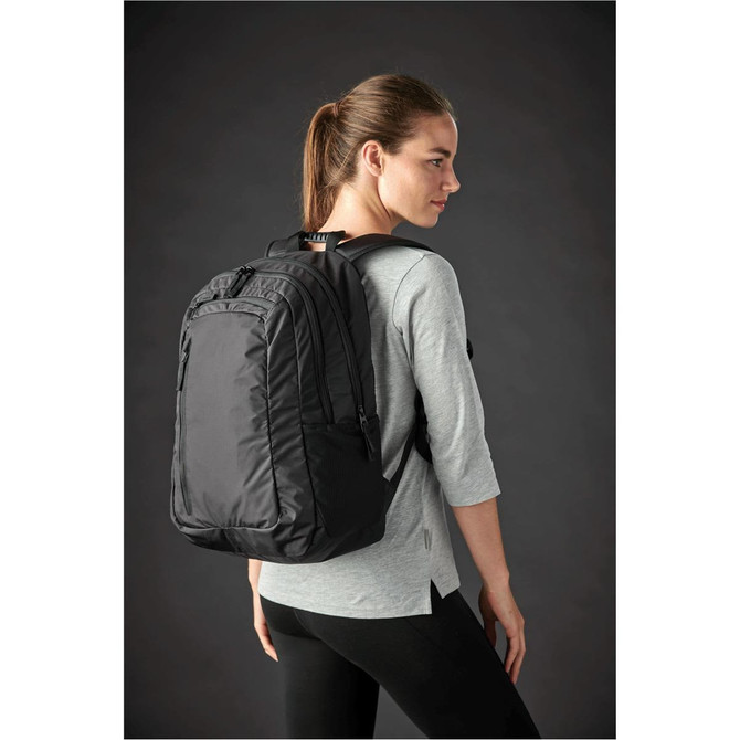 A black laptop bag is worn on the back of a woman, featuring multiple compartments and a sleek design.