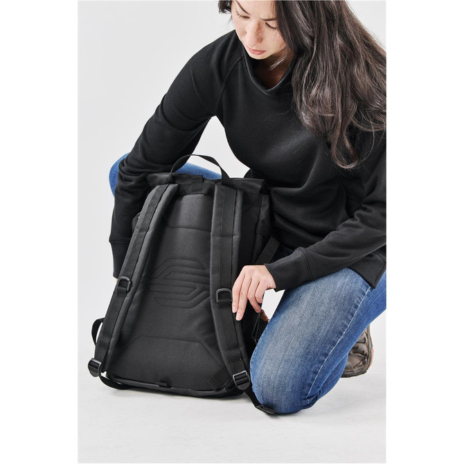 A black Chappaqua backpack is being adjusted by a person dressed in a black top and jeans, featuring a logo on the back.