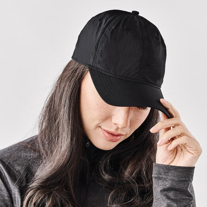 A black cap is worn by a person with long hair. The cap features a logo on the front.