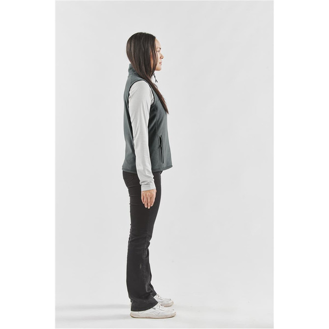 A side view of a women's fleece vest in dark grey, worn over a light long-sleeve top, with zipped pockets.