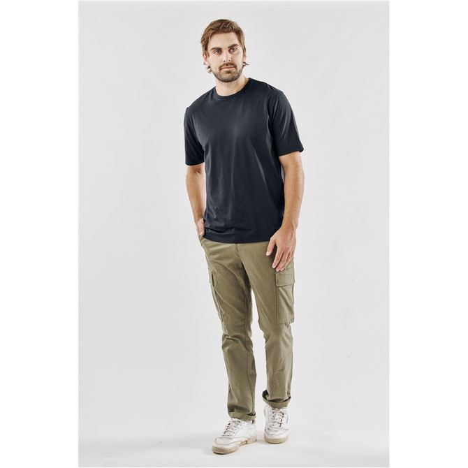 A man wearing a black T-shirt and khaki cargo pants stands against a neutral background. The T-shirt features a logo.