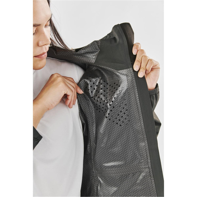 A woman examines the interior of a women's rain jacket in dark green, featuring mesh detailing and ventilation.