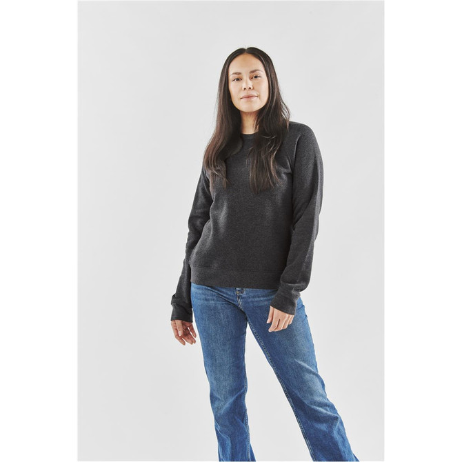 A woman stands wearing a dark grey fleece crew neck jumper with long sleeves and blue jeans.