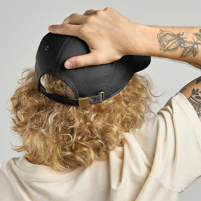 A black cap made from organic and recycled cotton, featuring a logo and worn casually with curly hair visible.