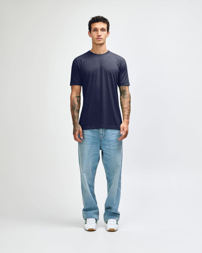 A model stands wearing a navy American Apparel Tri-Blend T-shirt and light blue jeans, with white shoes.