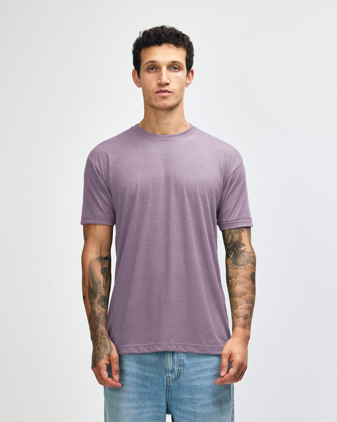 A man wearing a purple American Apparel tri-blend T-shirt paired with light blue jeans, featuring visible tattoos on his arms.