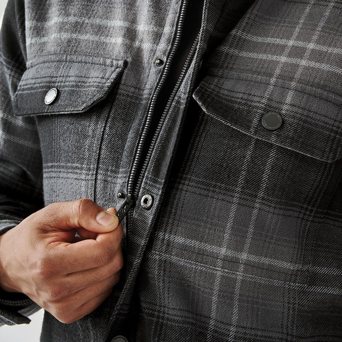 A men's plaid jacket in shades of grey, featuring a Sherpa lining and front pockets, with a zipper being fastened.